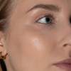 Nahaufnahme der strahlenden Haut einer Frau mit hellbraunem Haar und goldenem Ohrring, die mit LH Cosmetics Artistick Highlighter verschönert wurde.