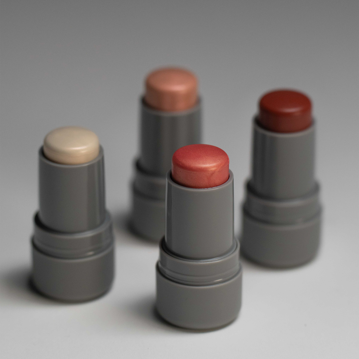 Vier graue Tuben von LH Cosmetics Artistick Highlighter in verschiedenen Farbtönen auf neutralem Hintergrund.