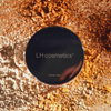 LH Cosmetics Infinity Filter Behälter auf einer Fläche mit verstreutem beigem und orangefarbenem Puder.