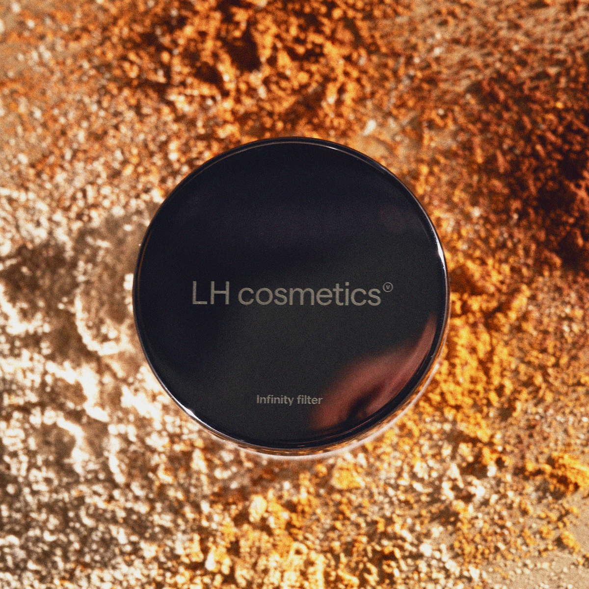 LH Cosmetics Infinity Filter Behälter auf einer Fläche mit verstreutem beigem und orangefarbenem Puder.