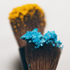 LH Cosmetics „On the go“-Pinselset: zwei Pinsel, einer mit hellblauem Puder, einer mit gelbem, vor einem einfarbigen Hintergrund.