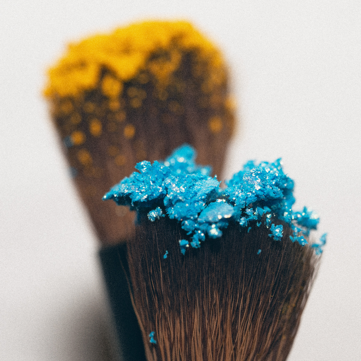 LH Cosmetics „On the go“-Pinselset: zwei Pinsel, einer mit hellblauem Puder, einer mit gelbem, vor einem einfarbigen Hintergrund.
