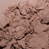 Nahaufnahme von LH Cosmetics The Single, loser hellbrauner Puder, der auf eine strukturierte Oberfläche gestreut ist.