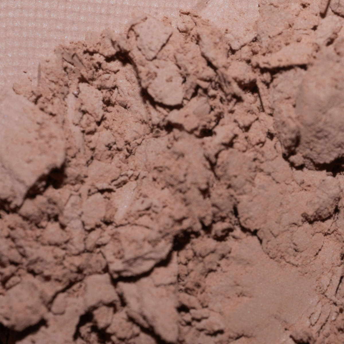Nahaufnahme von LH Cosmetics The Single, loser hellbrauner Puder, der auf eine strukturierte Oberfläche gestreut ist.