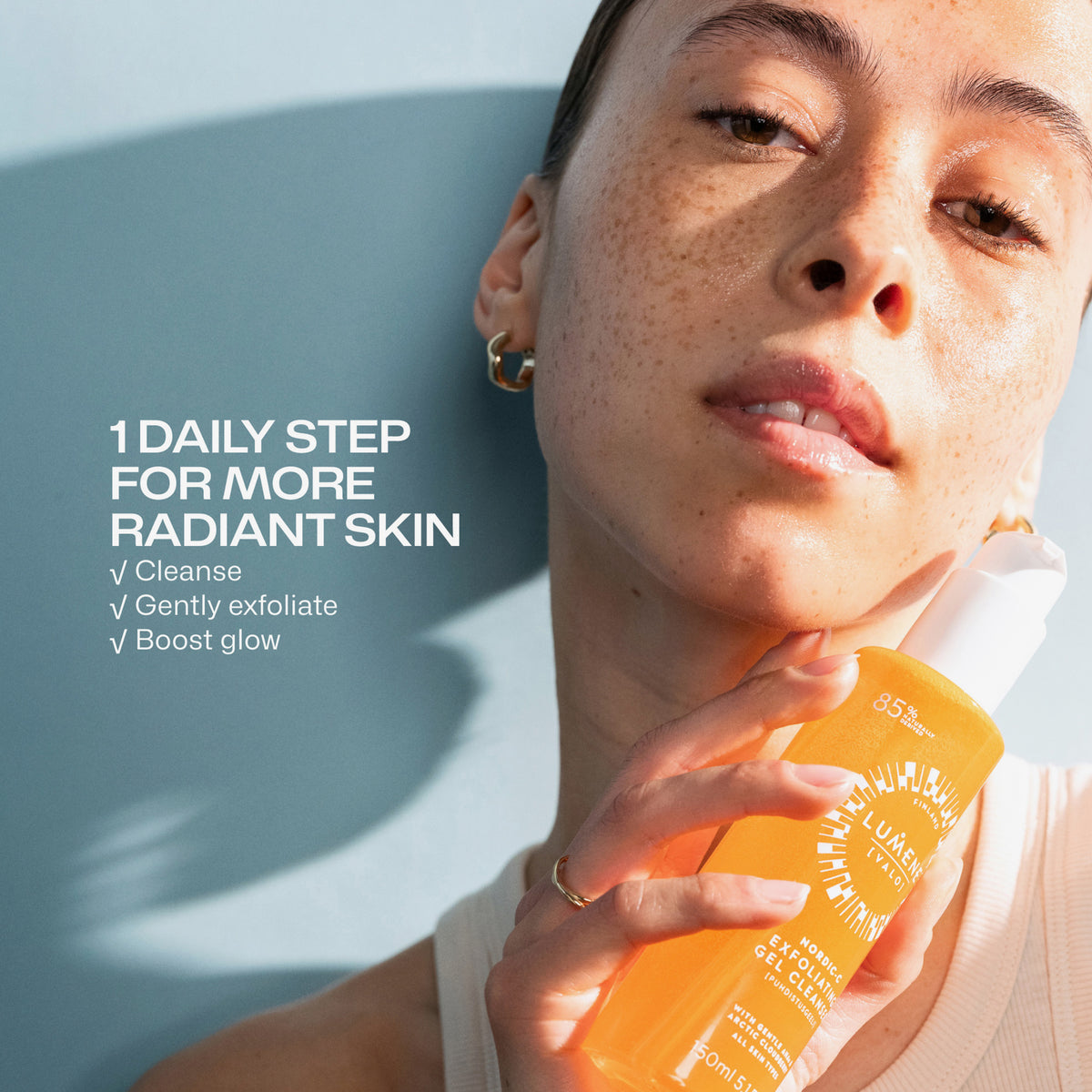 Eine Frau mit strahlender Haut hält eine Lumene Nordic-C [VALO] Exfoliating Gel Cleanser Flasche an ihre Wange, daneben sind Hautpflegetipps abgebildet.