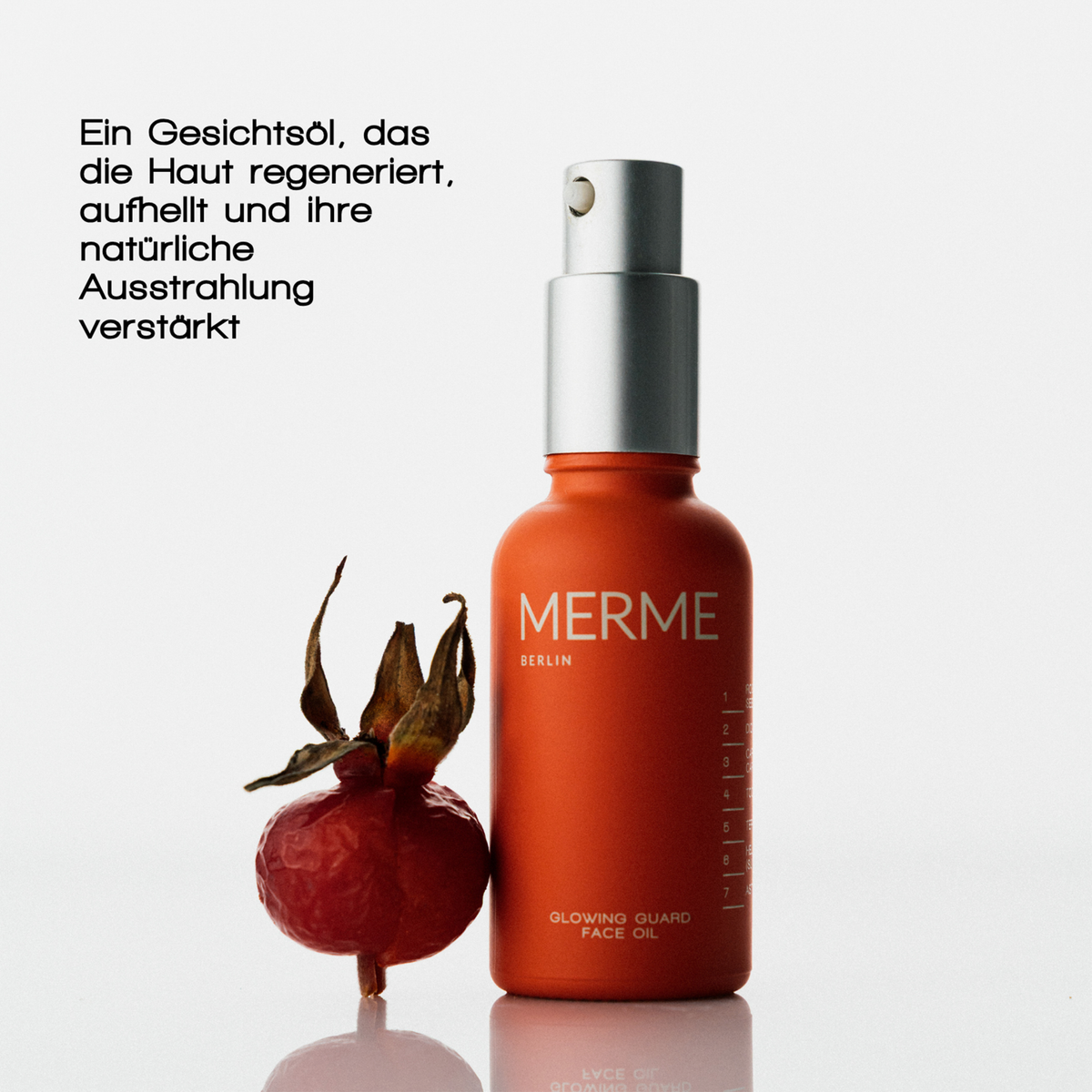 Die MERME Glowing Guard Face Oil Flasche mit Pumpe steht neben einer Hagebuttenfrucht, auf der ein deutscher Text die Vorteile für die Haut hervorhebt.