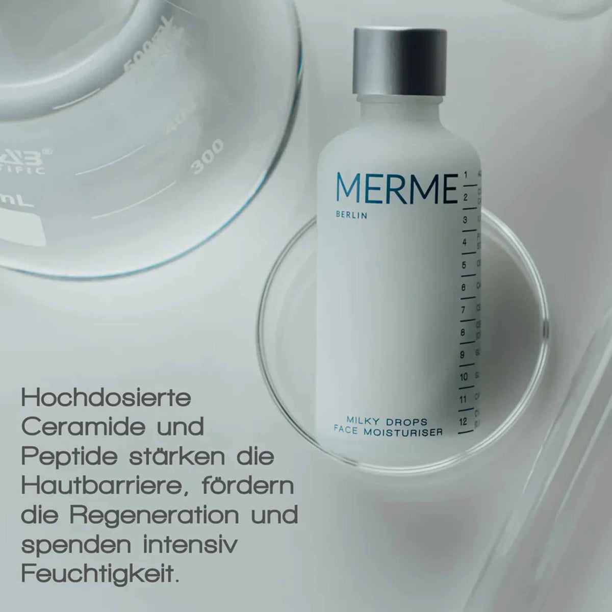 Eine Flasche MERME Milky Drops Face Moisturiser ruht in einer durchsichtigen Schale neben Laborglas.
