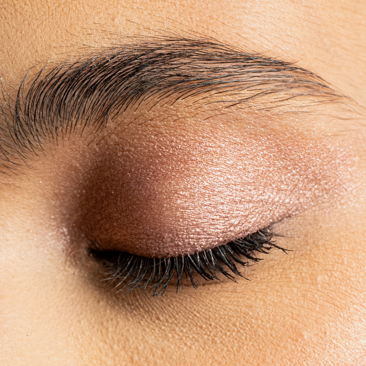 Nahaufnahme eines geschlossenen Auges mit schimmerndem rosé-bronzenem Lidschatten aus dem Mesauda Drawmatic Shadow in der Farbe Halo.