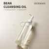 Eine durchsichtige Flasche von mixsoon Bean Cleansing Oil mit einem Pumpspender ist zusammen mit Öltropfen auf einem beigen Hintergrund abgebildet.