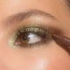 Nahaufnahme eines Auges mit schimmerndem grün-goldenem Augen-Make-up. Ein bronzefarbener Lidschattenstift betont den äußeren Augenwinkel.