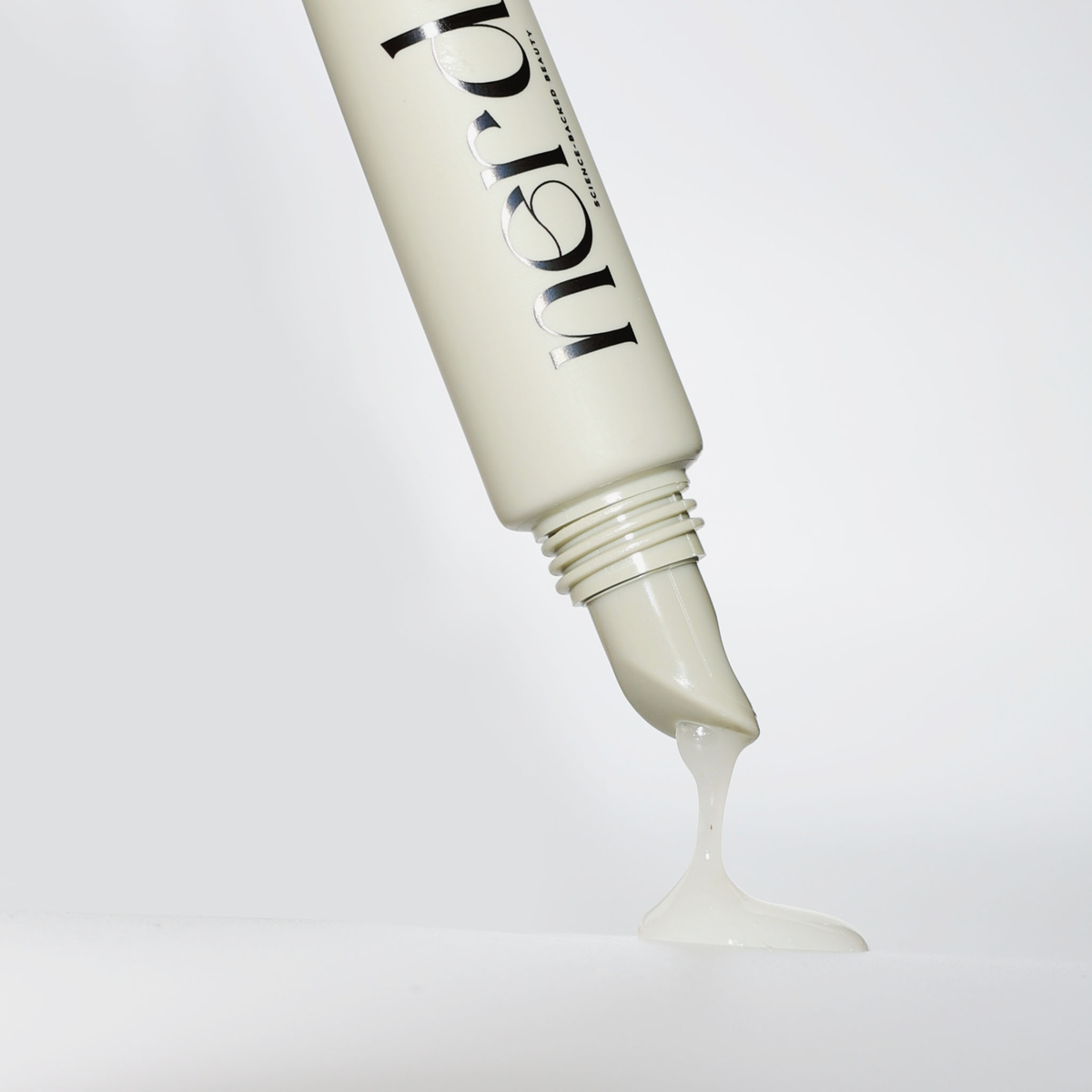 Beigefarbene Tube von NERDS. Peptide + Hyaluronic Acid Lip Treatment Original auf einem weißen Hintergrund, milchiger Lipgloss läuft heraus.