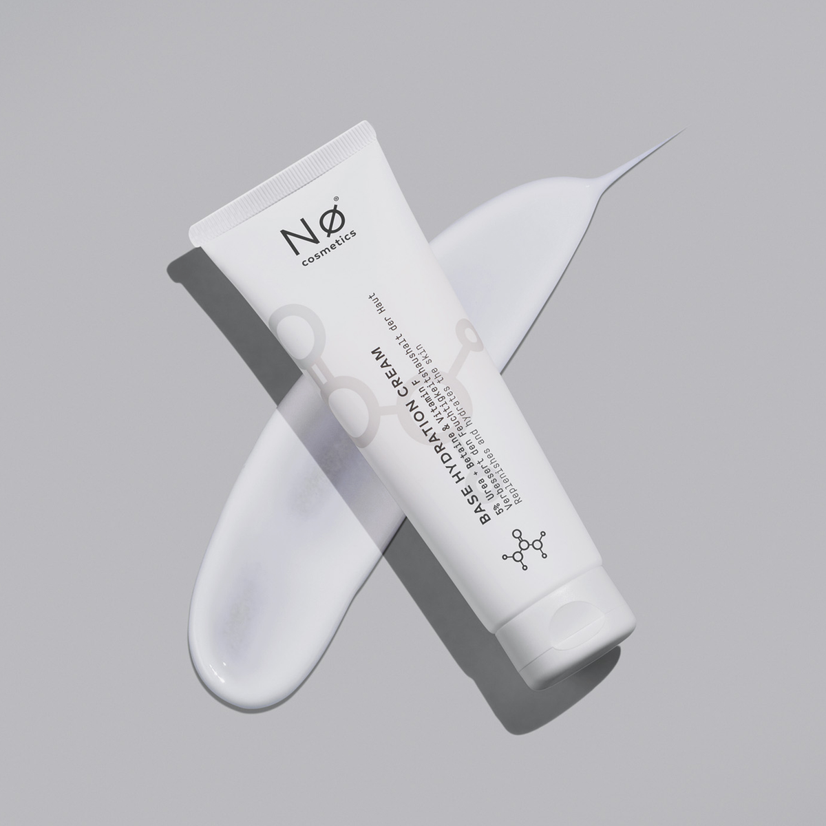 Basic tøday Base Hydration Cream von Nø Cosmetics in einer weißen Tube auf grauer Oberfläche mit darunter verschmierter Creme.