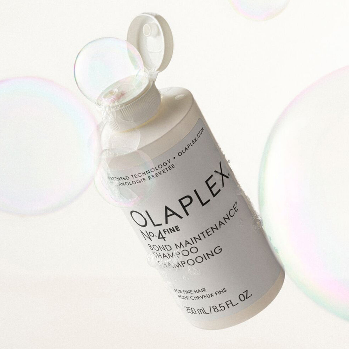 Offene schwebende Flasche N°4 FINE Bond Maintenance Shampoo von OLAPLEX zwischen zwei Blasen.