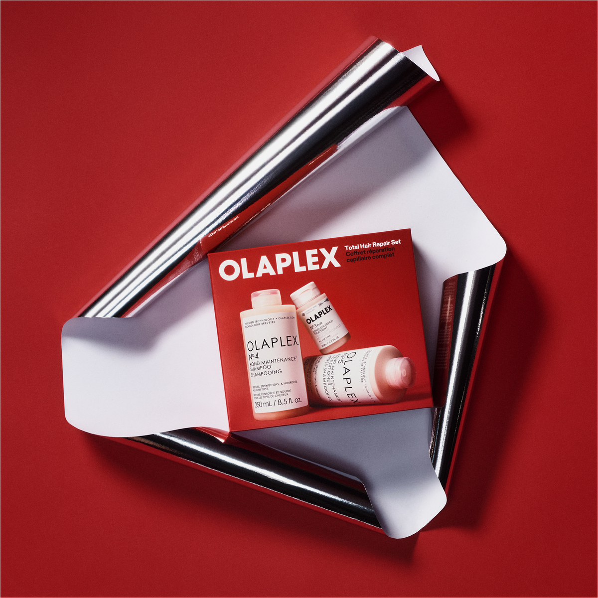 OLAPLEX Total Hair Repair Holiday Kit 2026 – Geschenkbox, verpackt in silberner Folie vor rotem Hintergrund.