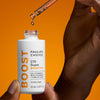 Eine Hand hält vor einem orangefarbenen Hintergrund eine Pipette über einer C15 Super Booster-Flasche und gibt einen Tropfen ab.