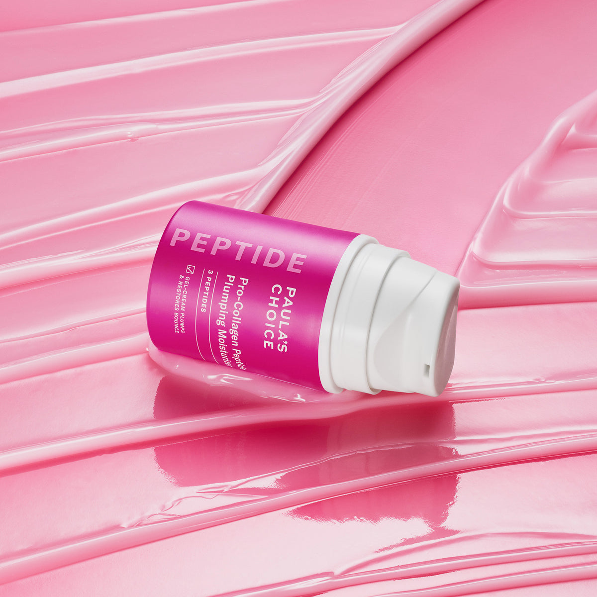Eine rosafarbene Flasche der Paula's Choice Pro-Collagen Peptide Plumping Feuchtigkeitscreme ruht auf einer glänzenden, rosafarbenen, strukturierten Creme-Oberfläche.