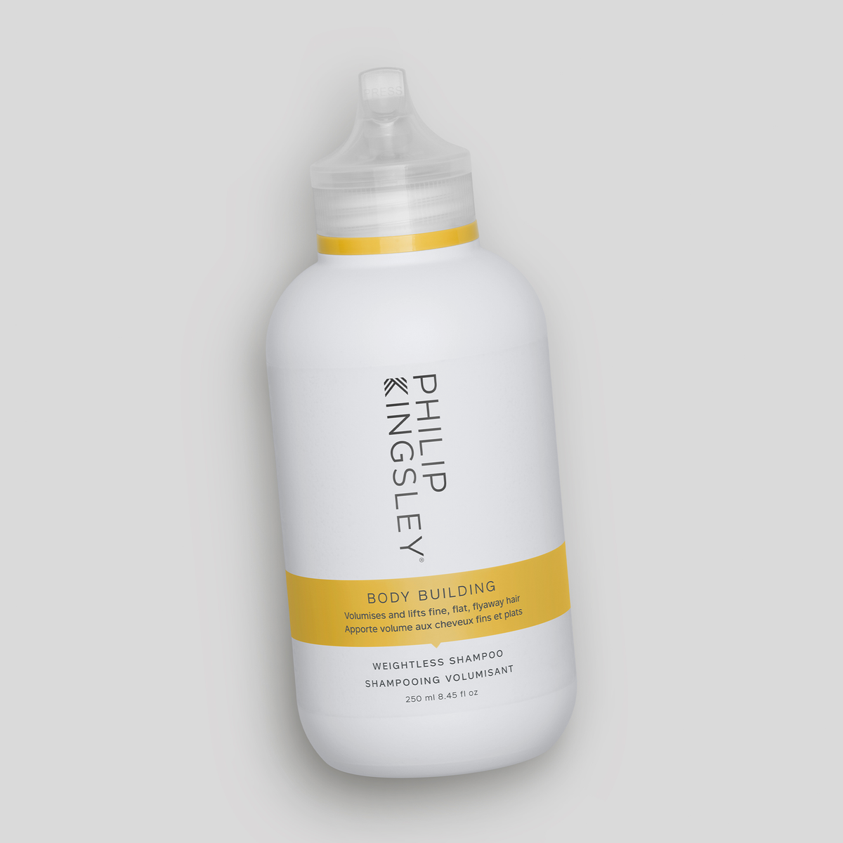 Philip Kingsley Body Building Shampoo in einer weißen Flasche mit gelbem Etikett, schräg auf einem hellgrauen Hintergrund abgebildet.