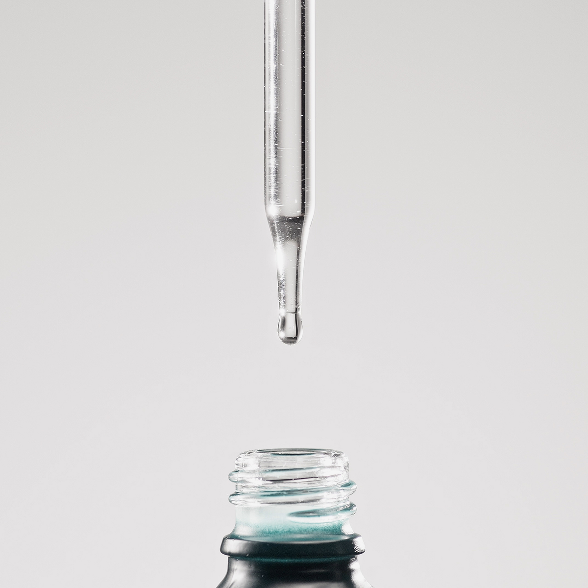 Ein einzelner Tropfen des „Philip Kingsley Density Preserving Scalp Drops“ fällt vor einer weißen Kulisse über die Flaschenöffnung.