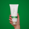 Eine Hand hält eine Tube „Philip Kingsley Flaky Itchy Scalp Conditioner“ vor einem grünen Hintergrund.