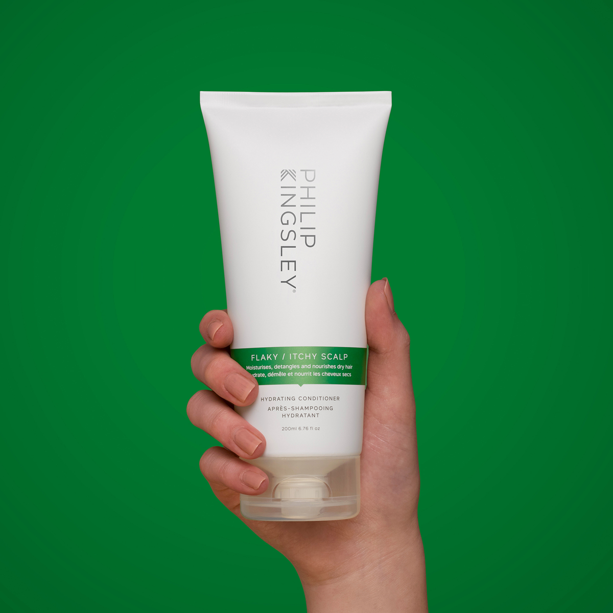 Eine Hand hält eine Tube „Philip Kingsley Flaky Itchy Scalp Conditioner“ vor einem grünen Hintergrund.