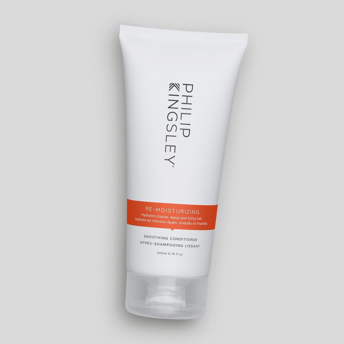 Eine weiße Tube „Philip Kingsley Re-Moisturizing Conditioner“ mit einem orangefarbenen Etikett auf grauem Hintergrund.