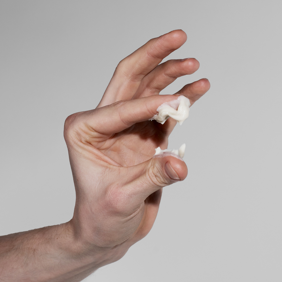 Eine Hand hält eine kleine Menge von Scandinavian Biolabs Firm Hybrid Clay zwischen ihren Fingern vor einem schlichten grauen Hintergrund.