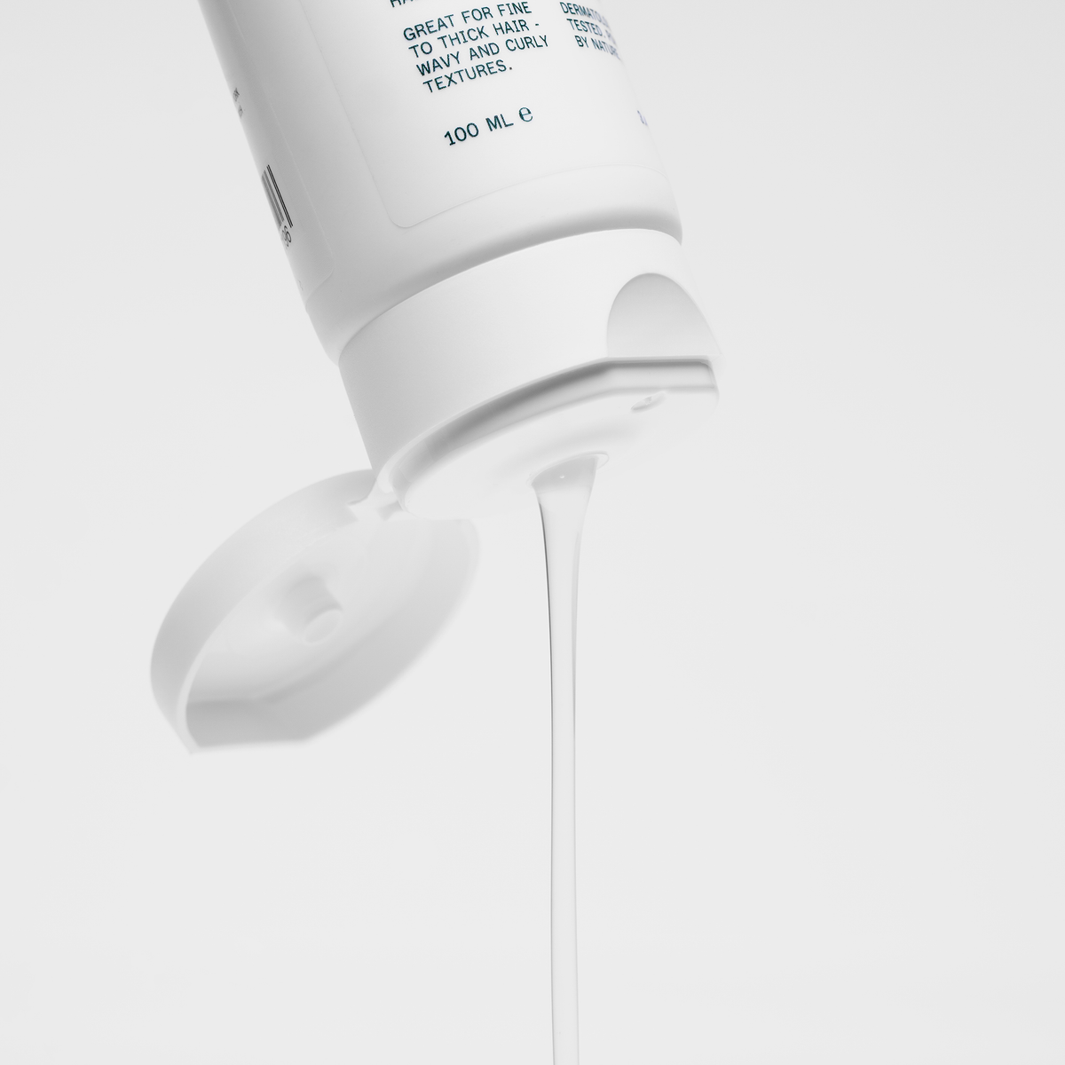 Eine weiße Flasche Scandinavian Biolabs Hair Styling Gel mit einem Flip-Cap offen spendet einen Strom von Gel vor einem weißen Hintergrund.