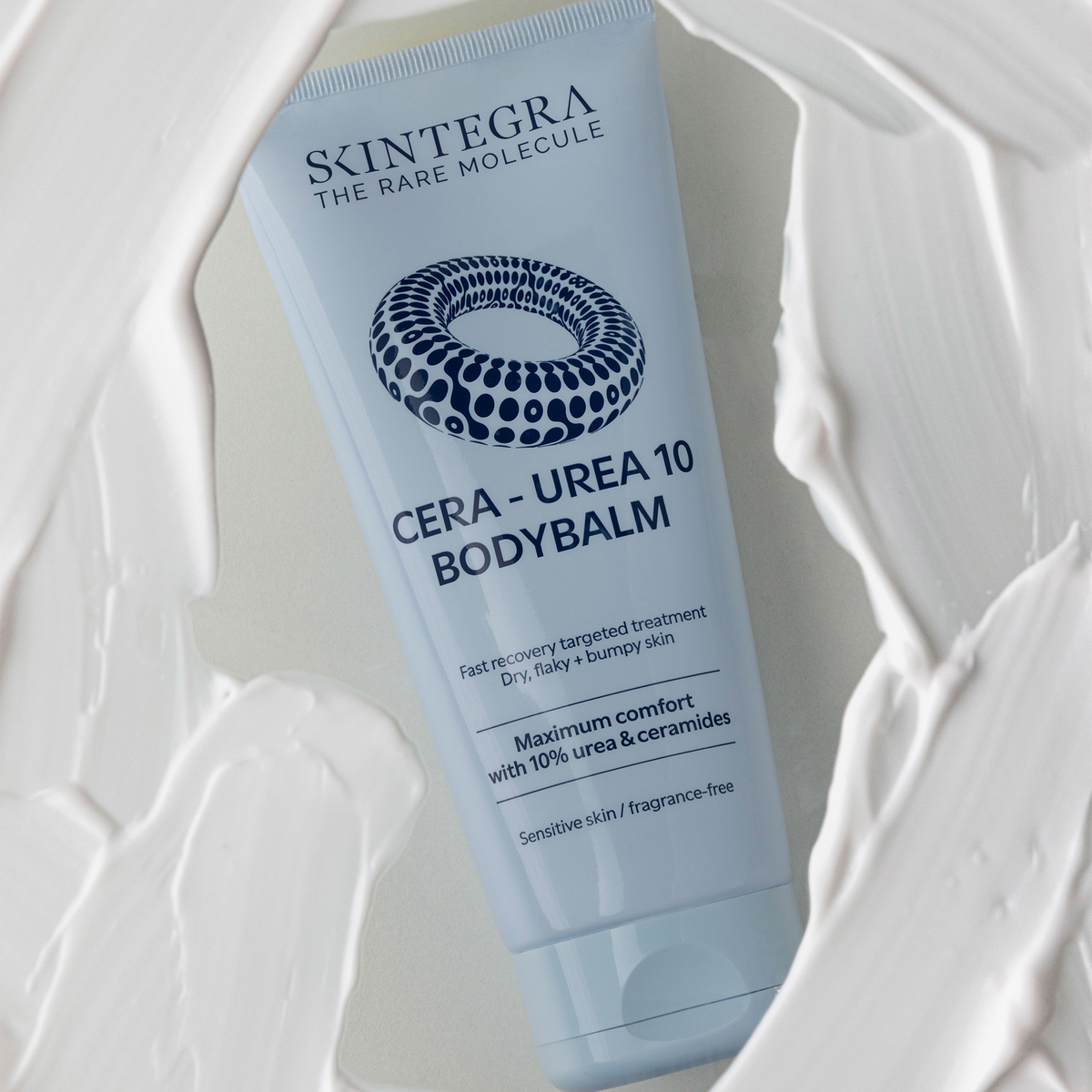 Eine Tube Skintegra Cera-Urea 10 Bodybalm, umgeben von einem Wirbel aus cremiger Lotion.