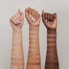 Drei hochgehaltene Unterarme zeigen die Farbtöne 1–15 der SWEED Glass Skin Foundation und verdeutlichen damit die Bandbreite der Hauttöne von hell bis dunkel.