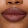 Nahaufnahme der Lippen mit dem geschmeidigen, dunkel-malvenfarbenen Lippenstift „SWEED Le Lipstick“, einer leichten Lücke zwischen den Vorderzähnen und der darüber sichtbaren Nase.