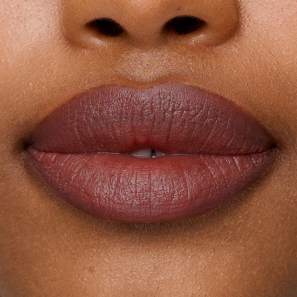 Nahaufnahme der Lippen mit dem geschmeidigen, dunkel-malvenfarbenen Lippenstift „SWEED Le Lipstick“, einer leichten Lücke zwischen den Vorderzähnen und der darüber sichtbaren Nase.