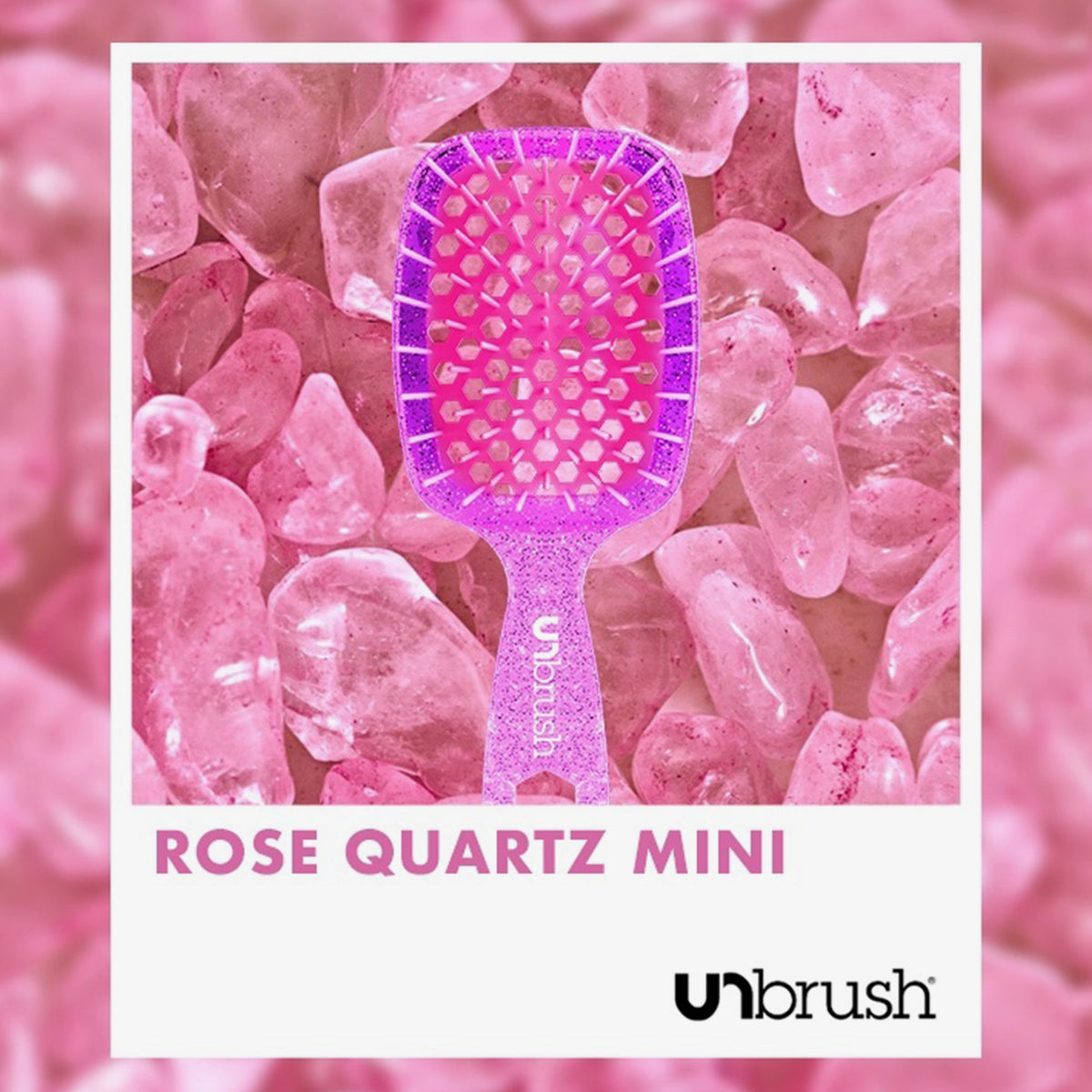 Eine rosafarbene Detangling-Haarbürste Mini von UNbrush ruht auf Rosenquarzsteinen, auf denen unten "ROSE QUARTZ MINI" und das UNbrush-Logo zu sehen sind.