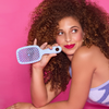 Frau mit lockigem Haar lächelt und hält die UNbrush Detangling Hair Brush vor einem hellrosa Hintergrund.