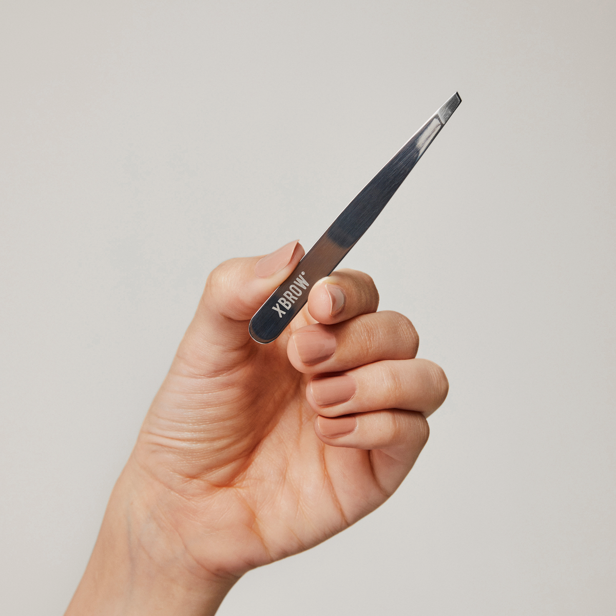 Eine Hand, die die XLASH Cult Classic Precision-Pinzette vor einem einfarbigen Hintergrund hält.