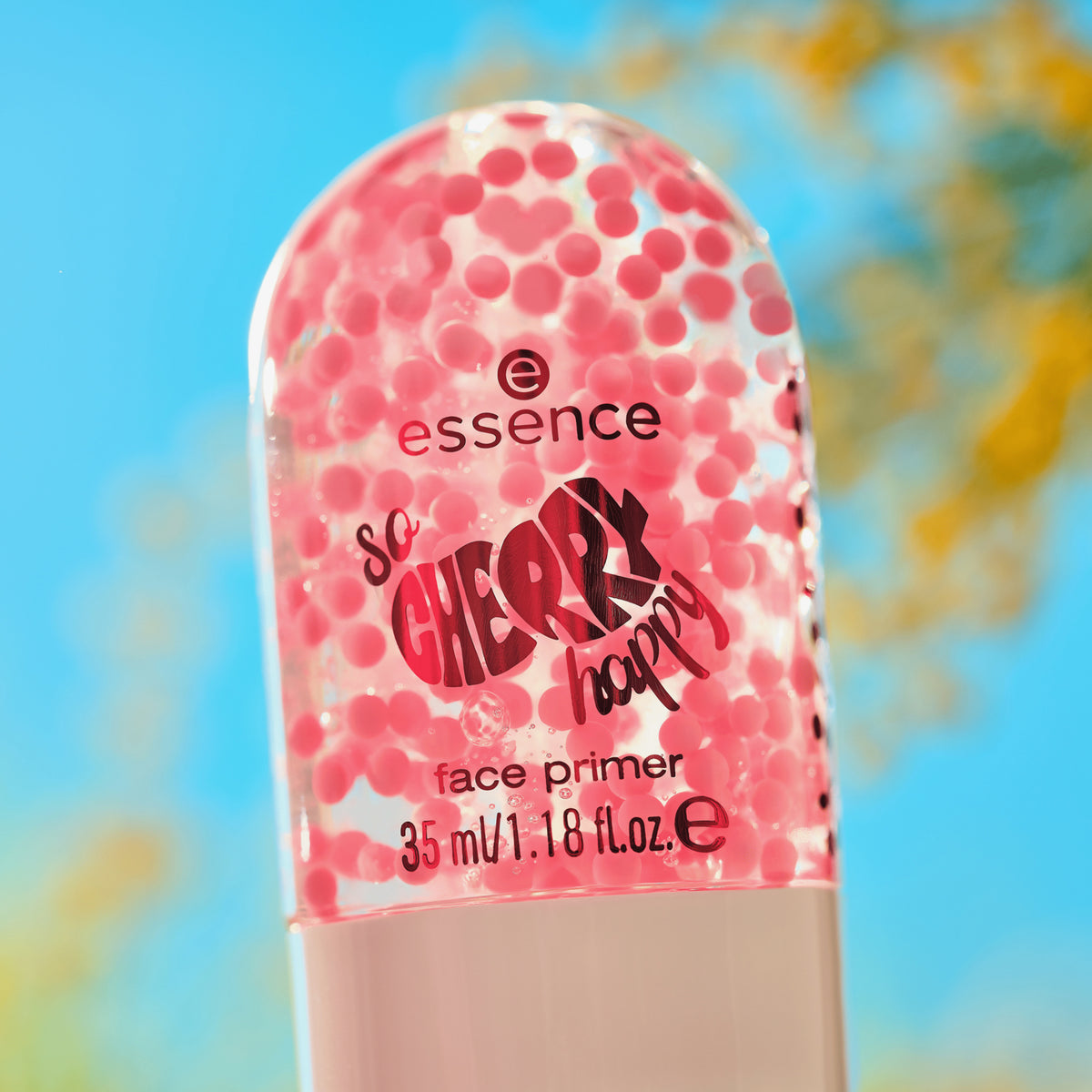 Nahaufnahme des SO CHERRY Happy Face Primer 01 mit rosa Perlen vor einem verschwommenen blauen und gelben Hintergrund.