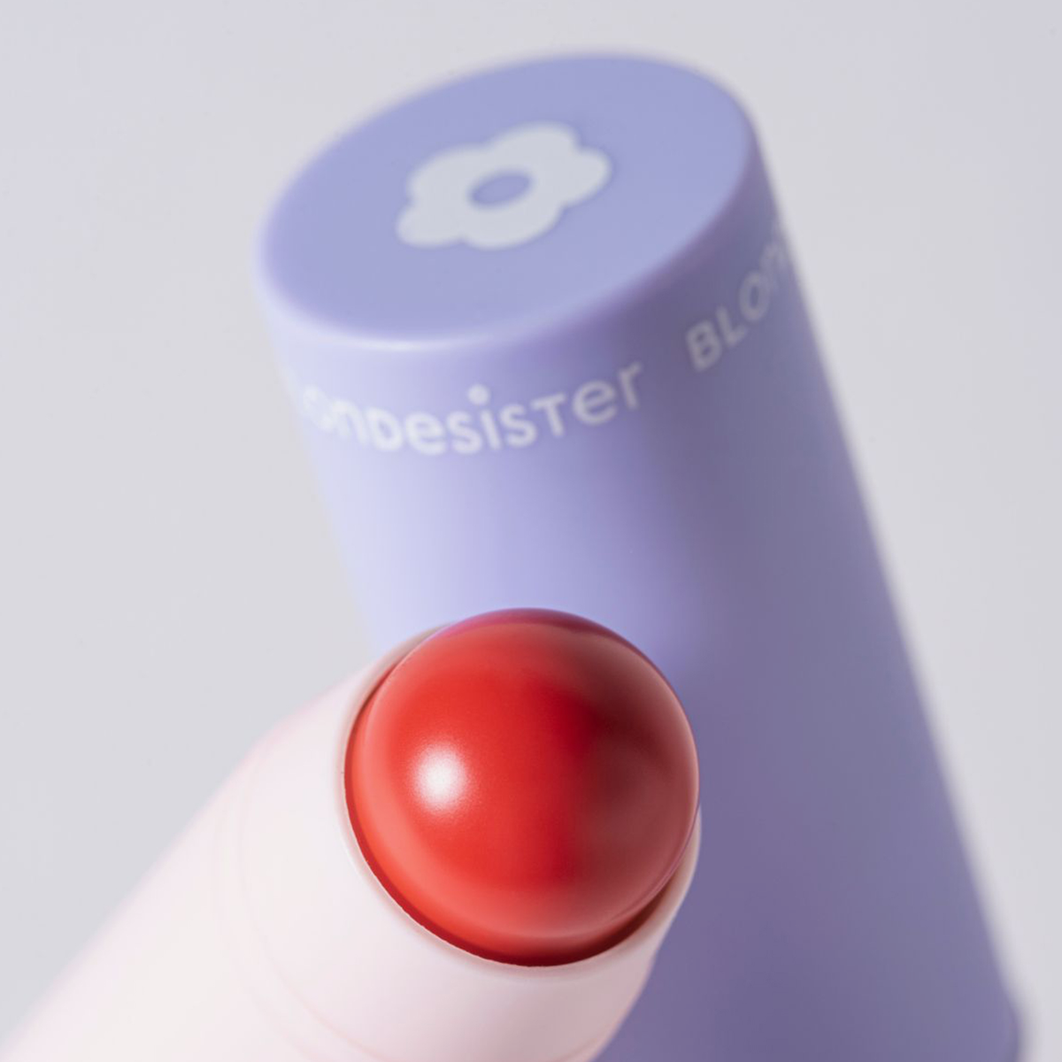 Eine Nahaufnahme von „BLONDESISTER 2 IN 1 IT’S UP TO YOU LIP OR CHEEK“ mit einer violetten Kappe und einem weißen Blumenmuster im Hintergrund.