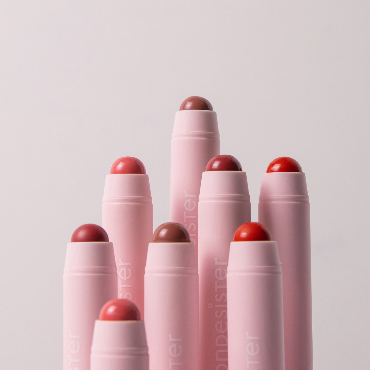 Acht BLONDESISTER 2-IN-1 „IT’S UP TO YOU“ Lippen- oder Wangenstifte in verschiedenen Rot- und Nude-Tönen, angeordnet auf einem hellen Hintergrund.