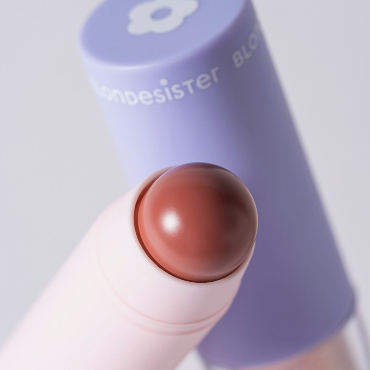 Eine Nahaufnahme des BLONDESISTER 2 IN 1 „IT’S UP TO YOU LIP OR CHEEK“-Stifts mit abgerundeter Spitze und einer violetten Kappe im Hintergrund.