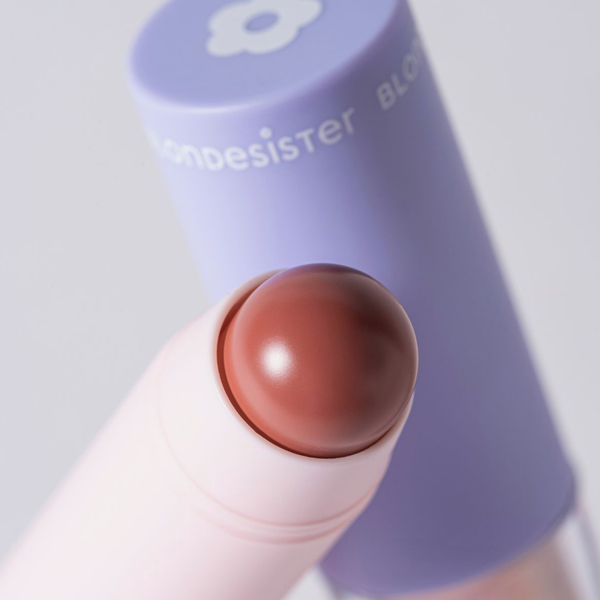 Eine Nahaufnahme des BLONDESISTER 2 IN 1 „IT’S UP TO YOU LIP OR CHEEK“-Stifts mit abgerundeter Spitze und einer violetten Kappe im Hintergrund.