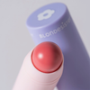 Nahaufnahme des rosa „2 IN 1 IT’S UP TO YOU LIP OR CHEEK“ von BLONDESISTER neben der violetten Tube.