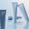 Drei Tuben „BLONDESISTER 2 IN 1 NATURAL BEAUTY TINTED CREAM SPF15“ stehen auf blauen Fliesen, eine davon spritzt Wasser.