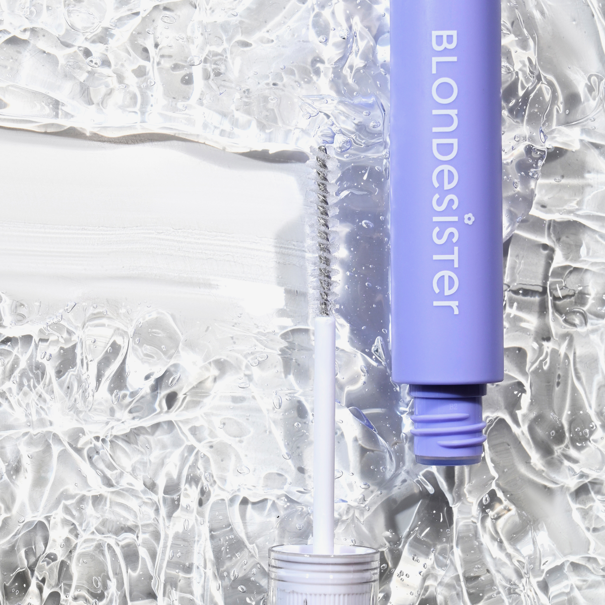 Ein violettes „3 IN 1 FIX&GO BROW GEL“ von BLONDESISTER mit einem weißen Pinsel auf einer durchsichtigen, strukturierten Oberfläche mit einem weißen Strich.