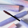 BLONDESISTER 4-IN-1-CLICK-&-TURN-MASCARA, abgebildet mit violetter Tube, Applikator und pastellfarbener Verpackung im Hintergrund.
