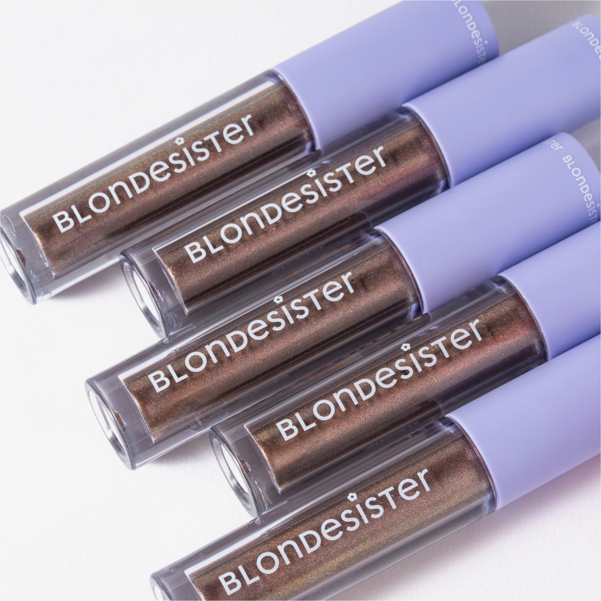 Fünf GLOWEYE-Lidschatten-Tuben von BLONDESISTER mit hellvioletten Verschlusskappen, diagonal auf einer weißen Fläche angeordnet.