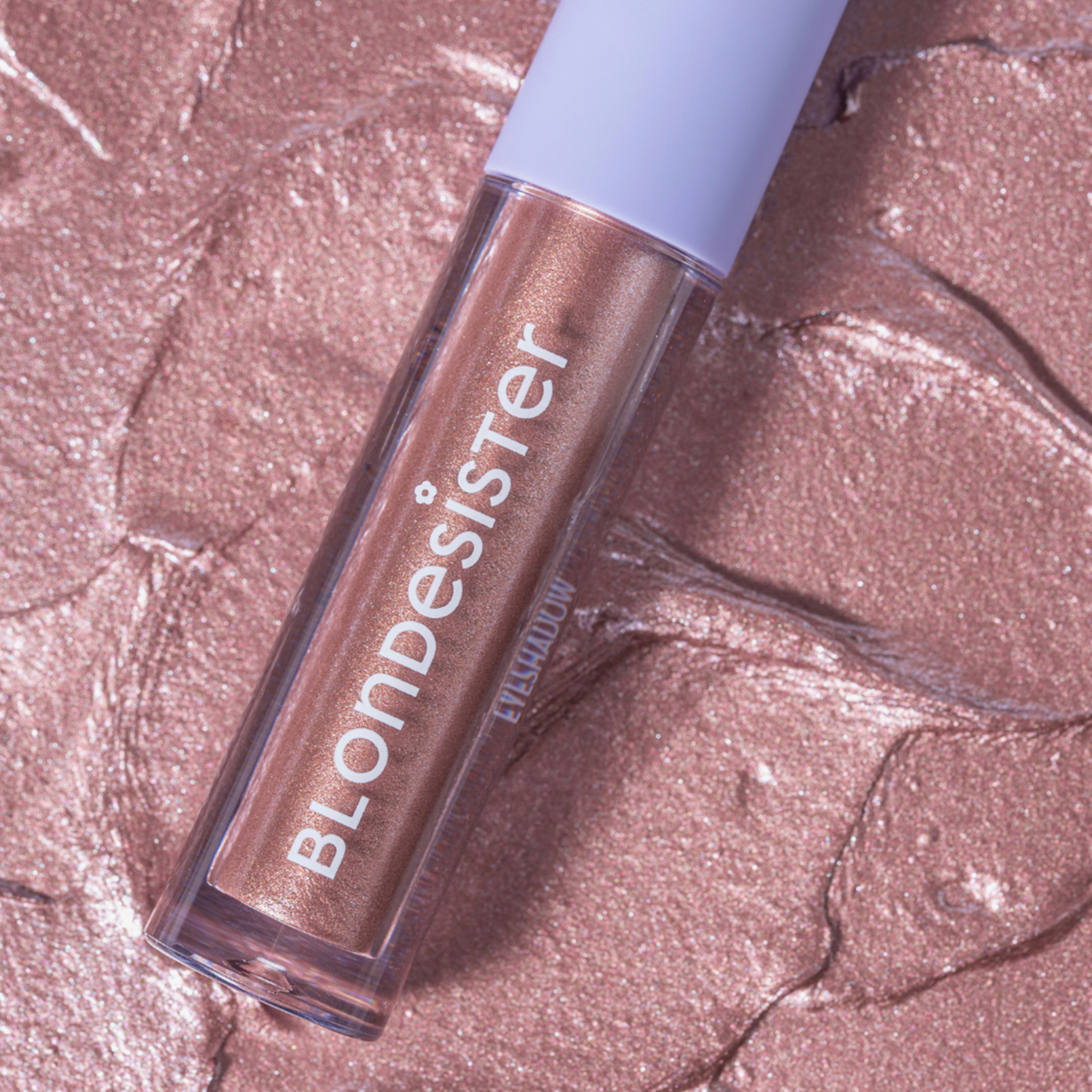 Ein GLOWEYE-Lidschatten von BLONDESISTER liegt auf einem strukturierten, schimmernden Roségold-Hintergrund, der farblich zum Lidschatten passt.