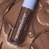 Tube mit BLONDESISTER GLOWEYE EYESHADOW in schimmerndem Bronze auf einer strukturierten, metallisch-bronzefarbenen Oberfläche.