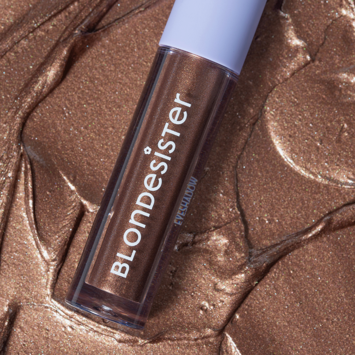 Tube mit BLONDESISTER GLOWEYE EYESHADOW in schimmerndem Bronze auf einer strukturierten, metallisch-bronzefarbenen Oberfläche.
