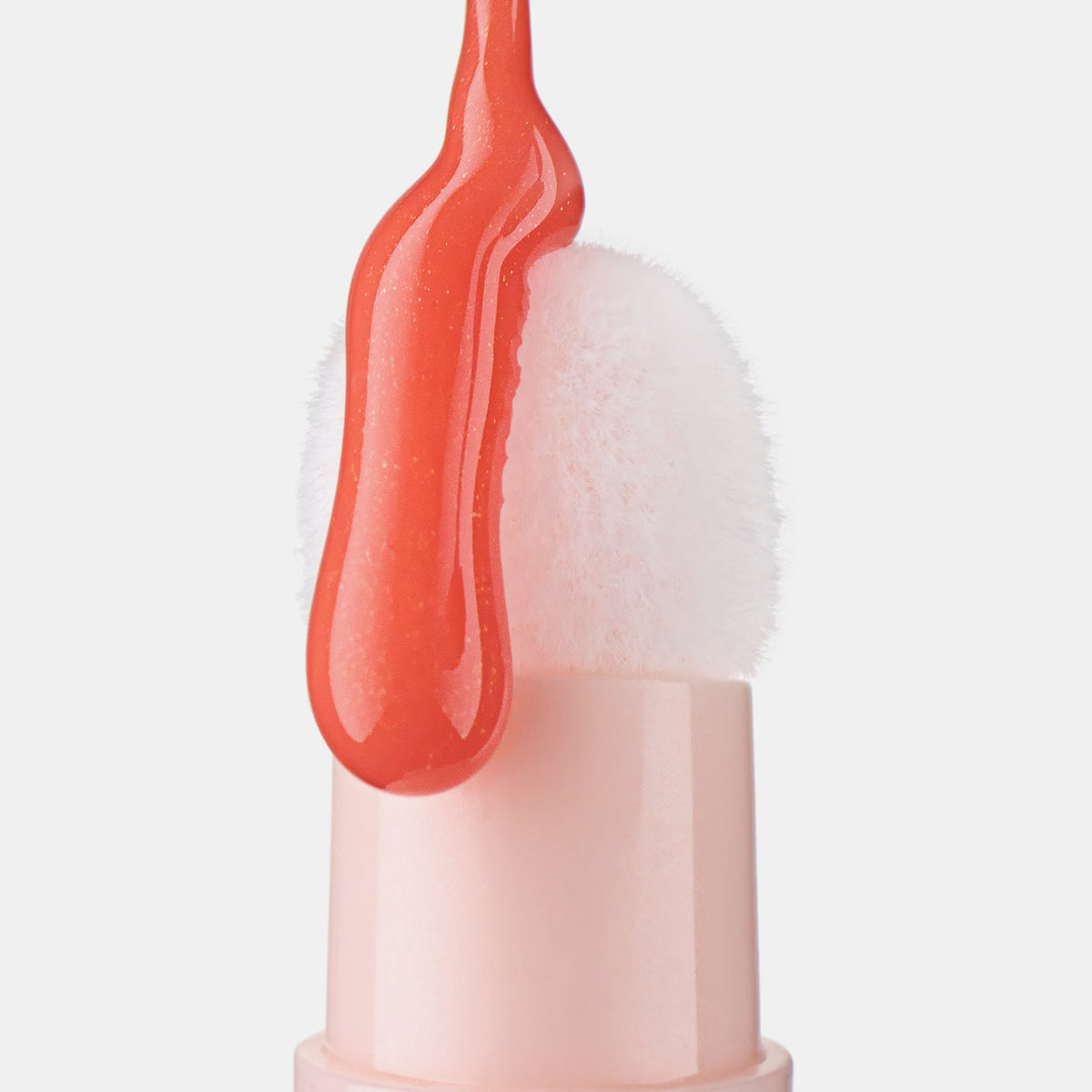 Eine Nahaufnahme des Colour Cushion Juicy Lip Oil von Catrice Cosmetics zeigt den flauschigen Applikator mit dem leuchtenden korallenroten Glanz.