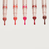 Fünf Catrice Colour Cushion Juicy Lip Oils nebeneinander, aus jedem Applikator tropft glänzendes farbiges Lip Oil in unterschiedlichen Nuancen.
