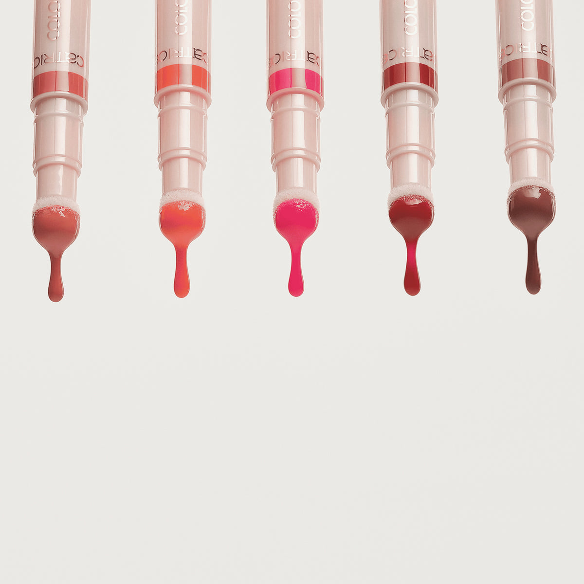 Fünf Catrice Colour Cushion Juicy Lip Oils nebeneinander, aus jedem Applikator tropft glänzendes farbiges Lip Oil in unterschiedlichen Nuancen.